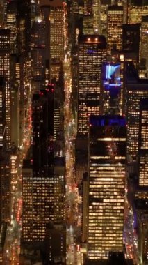 Gökdelenler ve hareketli caddelerle aydınlatılmış gökdeleri ve hareketli caddeleri olan canlı bir şehri gece hava görüntüsü gösteriyor.