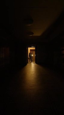Rahatsız edici derecede karanlık ve ürkütücü bir koridor, ilerideki açık bir kapıdan yayılan yumuşak bir parıltıyla aydınlanır.