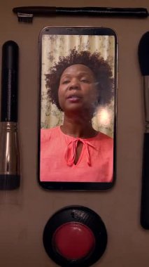 Çeşitli makyaj aletleri ve akıllı telefonuyla çevrili günlük güzellik rutiniyle mutlu bir kadın.