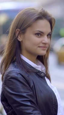 Şık ve kendine güvenen genç bir kadın, şehir ortamının canlı ve hareketli enerjisi arasında zarifçe poz verir.