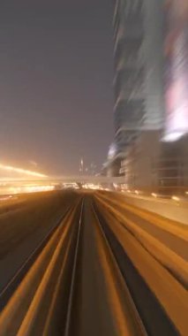 Gece ustalıkla aydınlatılmış canlı bir şehir ortamında kıvrılan tren raylarının puslu görüntüsü.