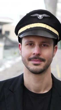 Akıllı bir şapka ve ceket giymiş gülümseyen bir pilot, hareketli havaalanında göreve hazır ve nazır.