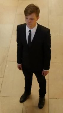 Tarz sahibi siyah takım elbiseli ve kravatlı genç bir adam ışıl ışıl bir ortamda poz verirken kendine güvenir.