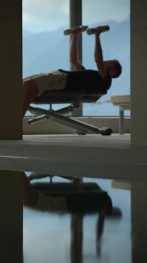 Modern, gösterişli bir spor salonunda yansıtıcı yüzeyler içeren bir bankta özenle egzersiz yapan bir birey.