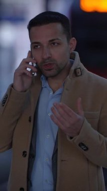 Şık giyimli bir adam telefonda konuşuyor ve hareketler yapıyor. Canlı şehir atmosferinin tadını çıkarıyor.