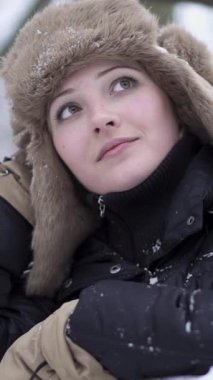 Hoş, sıcak bir şapka ve şık bir ceket giymiş düşünceli genç bir kadın, durgun, karlı bir manzaranın ortasında duruyor.