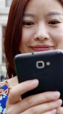 Akıllı telefonuyla gülümseyen bir kadın canlı bir şehir ortamında modern bir bağlantı sergiliyor.