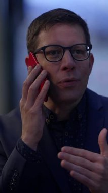 Gözlüklü şık bir adam açık havada konuşurken bir telefon görüşmesi yapar ve kendine güvenini yayar.
