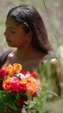 Huzurlu bir kadın zarif bir şekilde doğada duruyor, canlı bir buket gül tutuyor, huzur saçıyor.