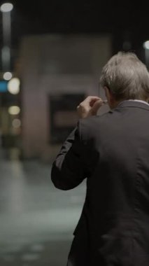 Keskin takım elbiseli bir adam gecenin karanlığında loş caddelerde tek başına yürür ve kasvetli bir atmosfer yaratır.