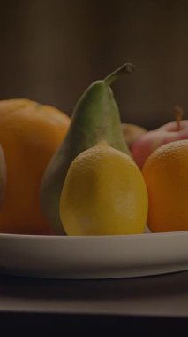 Armut, limon ve elma gibi canlı meyveler beyaz bir tabakta güzelce yerleştirilmiş.