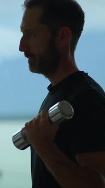 Bir adam ağırlık tutarken siluetlenir, muhteşem bir arka plan karşısında zindeliğini güzelce gösterir.