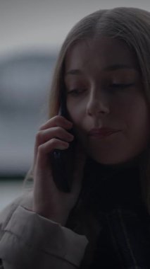 Genç bir kız anlamlı bir telefon görüşmesi yapıyor, canlı bir şehir zeminine karşı derin düşüncelerini sergiliyor.