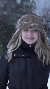 Sıcak bir kış şapkası ve palto giymiş neşeli genç bir kız, kar tanelerinin arasında sevinçle parıldıyor.