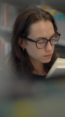 Canlı bir kütüphane ortamında yoğun bir konsantrasyon sergileyen, bir kadın, kendini meşgul edici bir kitaba kaptırdı.