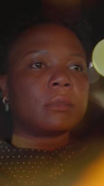 Bir kadın düşünceli bir şekilde gece boyunca arabasının camından dışarı bakar, dışarıdaki canlı şehir ışıklarından büyülenir.