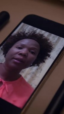 Güzel kıvırcık saçlı neşeli bir kadın akıllı telefonuyla zarif bir şekilde yakalanmış canlı bir atıştırmalıktan hoşlanır.