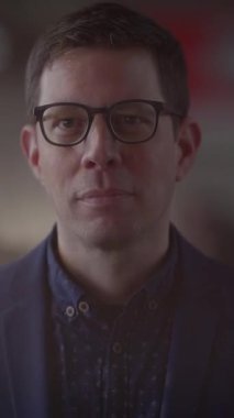 Kendini adamış bir adam, gözlük takıyor, çağdaş bir ortamda güven ve profesyonellik yayıyor.