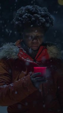 Karla kaplı bir kış gecesinde elinde kırmızı bir mum tutan bir insan, soğuk bir ortamda sıcaklık uyandırıyor..