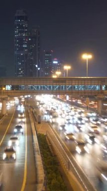 Işıklı gökdelenlerin altında akan trafik yoğunluğunu güzel bir şekilde yansıtan canlı bir gece sahnesi.