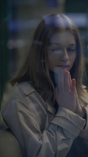 Une jeune femme réfléchie, les yeux fermés et les mains en prière, se dresse dans un contexte urbain saisissant