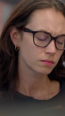 Çağdaş bir ofis ortamında, gözlüklü genç bir kadın düşünceli ve derin düşüncelere dalmış, muhtemelen stresli görünüyor.