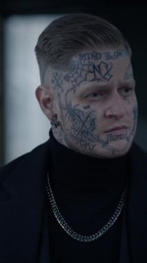 Karmaşık dövmelerle süslenmiş bir adam siyah bir balıkçı yaka giyerken çarpıcı ve unutulmaz bir varlık sergiler.