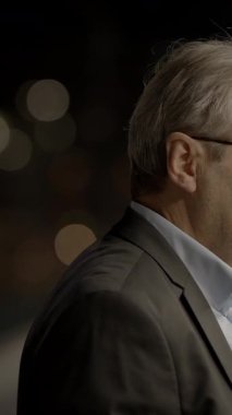 Takım elbiseli düşünceli bir adam güzel Bokeh ışıklarıyla çevrili, hareketli bir şehir gecesinde hayatı düşünür.