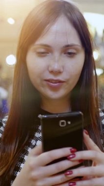 Parlak bir gülüşü olan genç bir kadın akıllı telefonunu kontrol eder. Etrafı parlak ve çağdaş bir çevreyle çevrilidir.