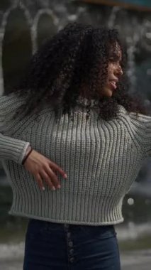 Bir kadın rahat bir süveter içinde neşeli bir şekilde gülümser, doğa güzelliğiyle çevrili güzel havanın tadını çıkarır.