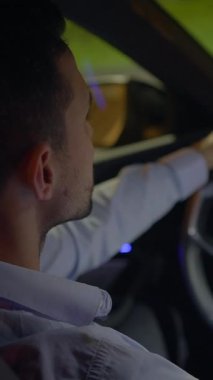 Gece şehirde gezen bir adam, canlı şehir ışıkları ve lüks modern araba iç mekanları tarafından vurgulanmış.