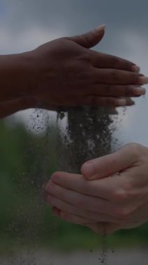 Hareketli ve güçlü bir birlik tasviri, sakin ve rahatlatıcı bir arka planda nazikçe kum tutan elleri gösteriyor.