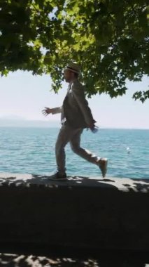 Yeşillik ve pırıl pırıl mavi suyla çerçevelenmiş, resmedilmiş bir rıhtımda rahatça gezinen bir adam.