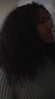 Bir kadın profili zarif bir şekilde sergiliyor çarpıcı kıvırcık saçlarını yumuşak, sessiz ve nazik bir ışıkla aydınlatıyor.