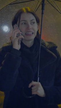 Bardaktan boşanırcasına yağan yağmurda elinde parlak bir şemsiye tutan bir kadın önemli bir telefon görüşmesi yaparken görünür bir şekilde endişeleniyor.
