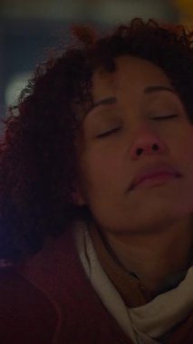 Güzel kıvırcık saçlı sakin bir kadın, gece saatlerinde hafifçe aydınlatılmış bir şehirde yansıtılır.