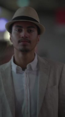 Şık bir adam canlı bir şehir ortamında şık bir takım elbise giymiş ve şapka takıyor.