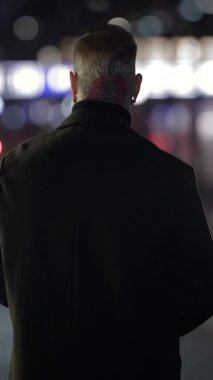 Issız bir figür, şehir ışıklarının bulanık zemininin önünde duruyor. Entrika ve yalnızlığı çağrıştırıyor.