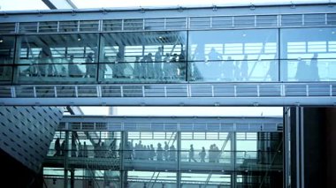 Pırıl pırıl cam bir yapı, çeşitli insanların hareketli bir geçiş bölgesinde ustalıkla yol almalarını gösteriyor.