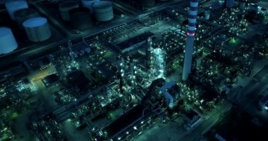 Geceleri aydınlık bir petrol rafinerisinin hava manzarası bacalar, şehir manzarası ve modern teknolojiyle