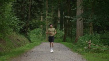 Bir insan, sakin bir orman içinde canlı, yemyeşil bir çim ile çevrili çakıl yolu boyunca koşuyor.