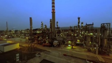 Alacakaranlıktaki endüstriyel petrol rafinerisinin panoramik manzarası. Aydınlatılmış makineler ve önde gelen bacalarla..
