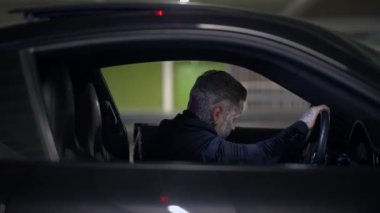 Yalnız bir şahıs karanlık bir otoparktan geçiyor, entrika ve belirsizlik ortamı yaratıyor.
