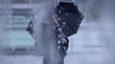 Yağmurda bulanık bir figür, şemsiye tutuyor, yağmurlu bir günün özünü derin duygularla yakalıyor.