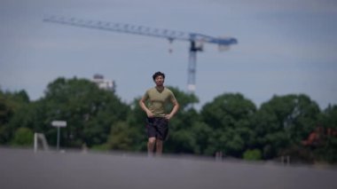 Genç bir adam enerjik bir şehirde, ağaçlar ve arka planda bir inşaat vinci ile koşar.