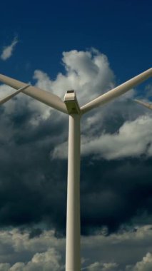 Üzerimizde dönen bulutlarla dolu kasvetli bir gökyüzüne karşı konumlanmış büyük bir rüzgar türbininin yakın görüntüsü.