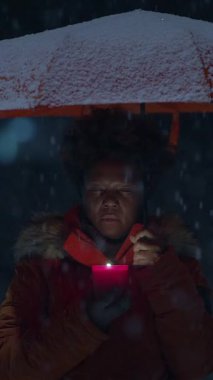 Bir kadın kar yağarken akıllı telefonuyla uğraşırken renkli bir şemsiyeyle korunuyor.