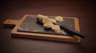 Taze kesilmiş muzlar şık, siyah bir mermer kesme tahtasına yerleştirilmiş, bıçakla tamamlanmış.