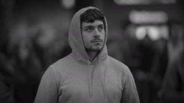 Kapüşonlu genç bir adam, neşeli ve coşkulu kalabalığın arasında sessizce duruyor.