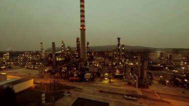 Alacakaranlıkta geniş bir petrol rafinerisinin hava görüntüsü endüstriyel karmaşıklık ve enerji üretimini gösteriyor..